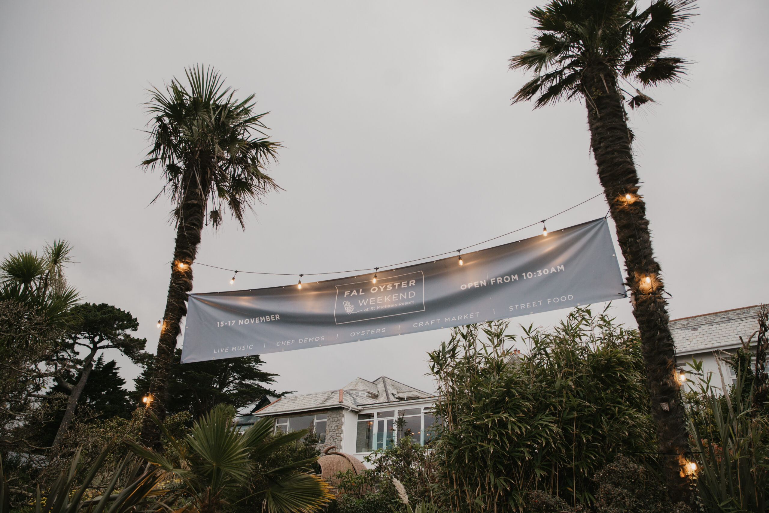 Twilight garden with tall palm trees, lush greenery, and a white draped canopy strung with warm lights, creating a serene tropical atmosphere.